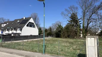 Leeres Grundstück mit Grasfläche und angrenzendem Wohngebäude mit Solaranlage auf dem Dach.