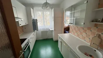 Funktionale Küche mit weißen Schränken, Spüle und grünem Linoleumboden.