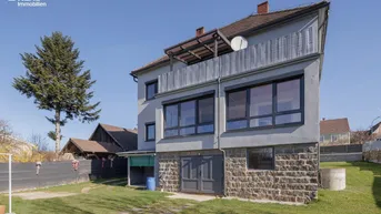Ansicht des Hauses von der Gartenseite mit Balkon und Steinsockel.