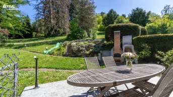 Großer Garten mit Terrasse, Grillplatz und Rutsche, umgeben von viel Grün.