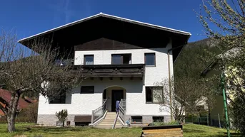 Vorderansicht eines Einfamilienhauses mit weißer Fassade und gepflegtem Vorgarten unter blauem Himmel.