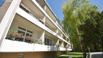 Mehrstöckiges Wohngebäude mit mehreren Balkonen und grüner Umgebung unter blauem Himmel.
