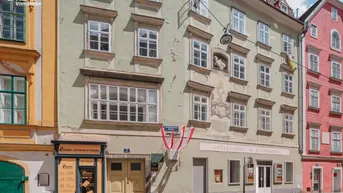 Historische Fassade eines Altbaus mit vielen Fenstern und Geschäften im Erdgeschoss an einer Straße.