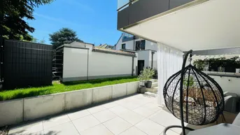 Große, sonnige Terrasse mit Fliesenboden und Hängesessel, umgeben von Grünflächen.