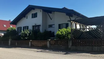 Weißes Einfamilienhaus mit Satteldach, grünen Fensterläden und einem Carport.