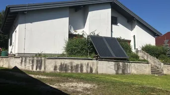 Rückansicht des Hauses mit Solaranlage auf dem Rasen und einer Betonmauer.