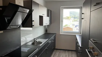 Moderne Küche mit dunklen Schränken, integrierten Geräten und Fenster.