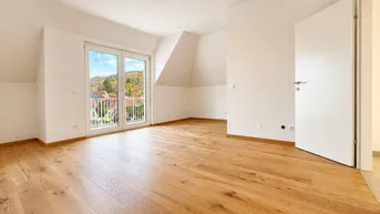 Helles Zimmer im Dachgeschoss mit Holzboden und Zugang zu einem französischen Balkon.