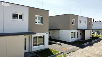 Moderne Reihenhäuser mit zweifarbiger Fassade und gepflegter Außenanlage unter blauem Himmel.