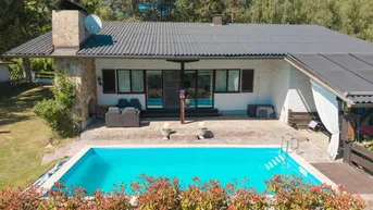 Ansicht des Hauses von hinten mit großem Pool, Terrasse und umgebender Natur.