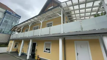 Langes, überdachtes Balkon- oder Terrassensystem mit Glasgeländer an der Fassade des Gebäudes.