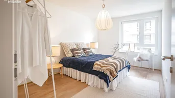 Helles Schlafzimmer mit Holzboden, großem Fenster und modernem Bett mit blauer Decke.