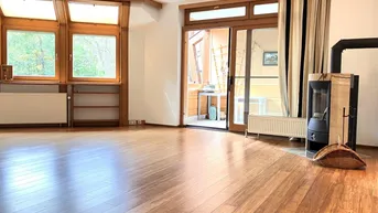 Helles Wohnzimmer mit Holzboden, großen Fenstern, einem modernen Kaminofen und Zugang zum Balkon.