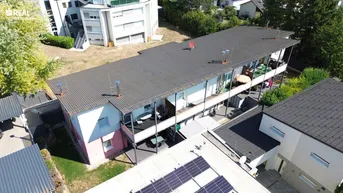 Luftaufnahme eines Mehrfamilienhauses mit mehreren Balkonen und umliegender Grünfläche unter einem Satteldach.