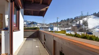 Sonniger Balkon mit Fliesenboden und Blick auf die schneebedeckten Berge und Skipisten.
