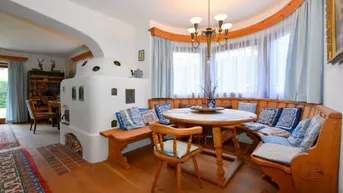 Traditioneller Essbereich mit Kachelofen, Holzbänken und einem runden Holztisch, ideal für gemütliche Mahlzeiten.