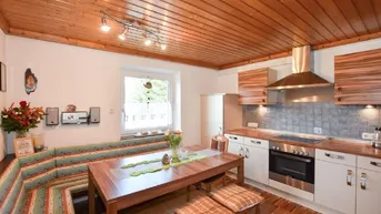 Gemütliche Wohnküche mit Holzbalkendecke, Essbereich und moderner Einbauküche.