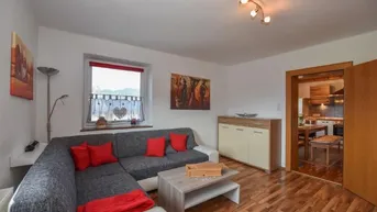 Helles Wohnzimmer mit gemütlichem Ecksofa, Laminatboden und Blick ins Grüne.