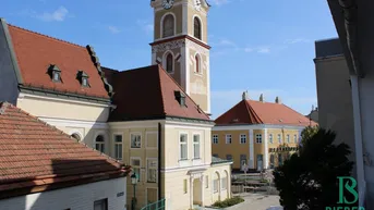 Blick auf eine historische Straße mit einer Kirche und traditionellen Gebäuden unter blauem Himmel.
