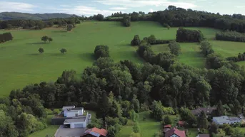 Luftaufnahme einer Wohnsiedlung mit modernen Häusern eingebettet in grüne Hügellandschaft.