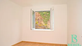 Ruhiges Schlafzimmer mit Holzboden und Fenster, das einen grünen Blick auf eine bewachsene Wand bietet.