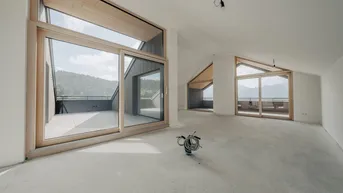Geräumiger, unfertiger Wohnbereich mit großen Fenstern, Holzdachschrägen und Zugang zur Terrasse mit Bergblick.