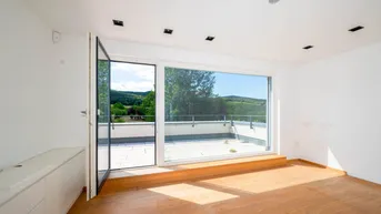 Heller Raum mit Holzboden und Zugang zu einer Dachterrasse mit weitem Blick auf die Landschaft.