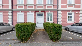 Vorderansicht des Gebäudes mit rosa Fassade, weißen Fenstern und gepflegten Hecken.
