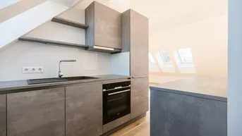 Moderne Küche in der Dachgeschosswohnung mit grauen Fronten, integriertem Backofen und Dachfenstern.
