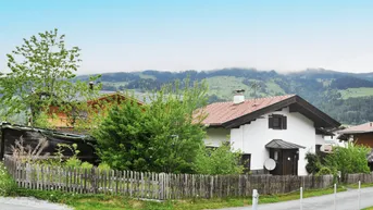 Traditionelles Haus mit Holzzaun und Blick auf die umliegende Berglandschaft und grüne Hügel.