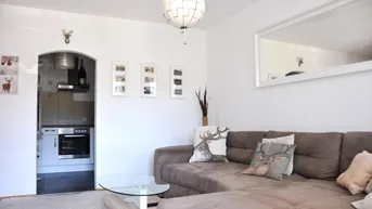 Gemütliches Wohnzimmer mit bequemer Couch, modernem Spiegel und Zugang zur Küche.