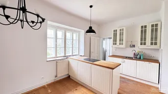 Helle Küche mit weißen Schränken, Holzarbeitsplatte und großem Fenster.
