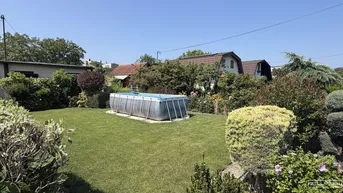Großer Garten mit Rasenfläche, Sträuchern und einem Aufstellpool unter blauem Himmel.