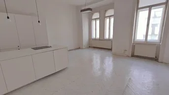Heller, offener Wohnbereich mit integrierter Küche und Fischgrätparkett, bereit zur Renovierung.