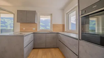 Moderne Küche mit grauen Schränken, Holzakzenten und Fenstern, die einen schönen Bergblick bieten.