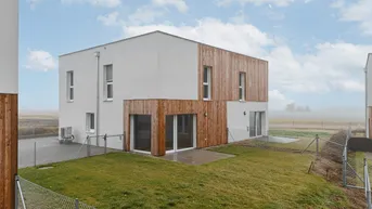 Modernes Reihenhaus mit Holzfassadenelementen und kleinem Gartenbereich in ländlicher Umgebung.