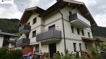 Mehrfamilienhaus mit mehreren Balkonen und traditioneller Architektur in grüner Berglandschaft.