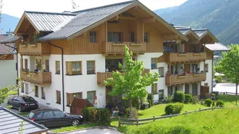 Traditionelles Wohnhaus im Chalet-Stil mit Holzbalkonen und Bergblick in grüner Umgebung.