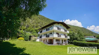 Großzügiges Anwesen mit Mehrfamilienhaus und weitläufigem Garten vor alpiner Bergkulisse.