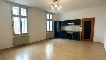Helles Zimmer mit Holzboden und integrierter Küchenzeile, ideal für offenes Wohnen.