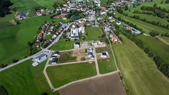Luftaufnahme eines Dorfes mit grünen Feldern und neuen Bauprojekten in ländlicher Umgebung.
