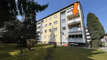 Ansicht des Mehrfamilienhauses mit Balkonen und grüner Umgebung an einem sonnigen Tag.
