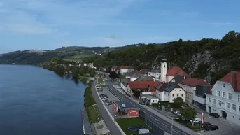 Panoramablick auf eine malerische Stadt am Flussufer mit grünen Hügeln im Hintergrund unter blauem Himmel.
