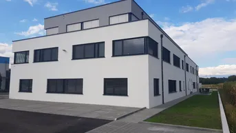 Modernes Bürogebäude mit weißer Fassade, grauen Akzenten und Jalousien unter blauem Himmel.