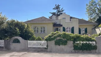 Gelbe Villa mit weißen Fensterrahmen, grünen Fensterläden und einem gepflegten Vorgarten.