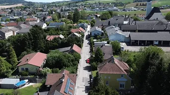 Panoramablick auf ein malerisches Dorf mit einer Kirche, umgeben von grünen Hügeln und Feldern unter blauem Himmel.