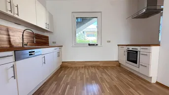 Leere Küche mit weißen Schränken, Holzarbeitsplatten, Spülmaschine und Dunstabzugshaube.