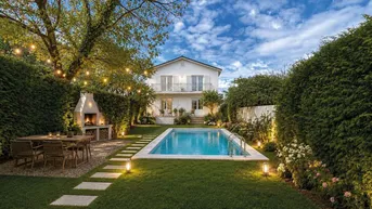 Gepflegter Garten mit Swimmingpool, Grillplatz und Essbereich im Freien, beleuchtet von Lichterketten.