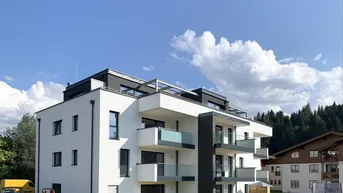 Modernes Mehrfamilienhaus mit weißer Fassade, Balkonen und einem kleinen Spielplatz im Grünen.