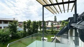 Moderner Balkon mit Glasgeländer und Blick auf die umliegende Bebauung und grüne Umgebung.